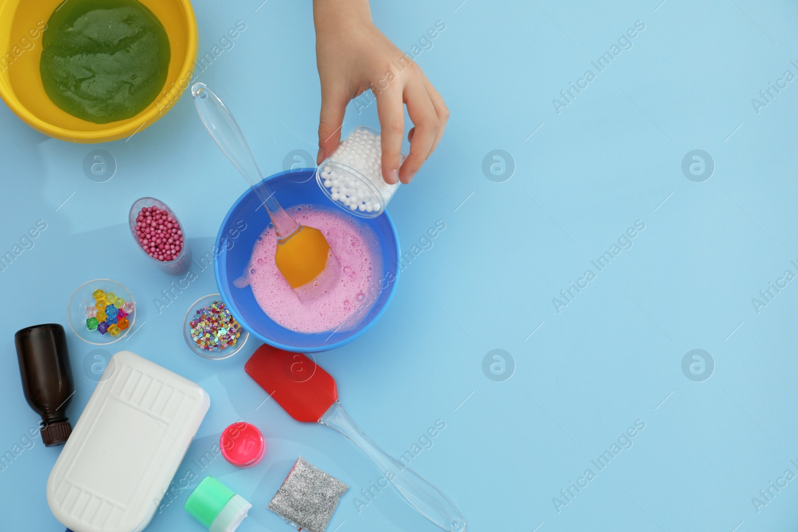 Photo of Little girl making slime toy on light blue background, top view. Space for text