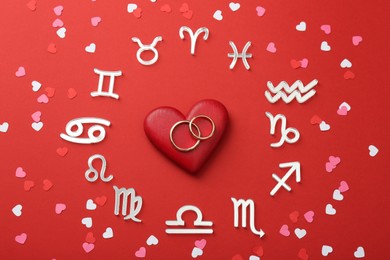 Photo of Zodiac signs, hearts and wedding rings on red background, flat lay
