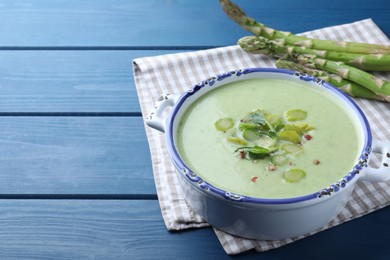 Photo of Delicious asparagus soup served on blue wooden table, space for text