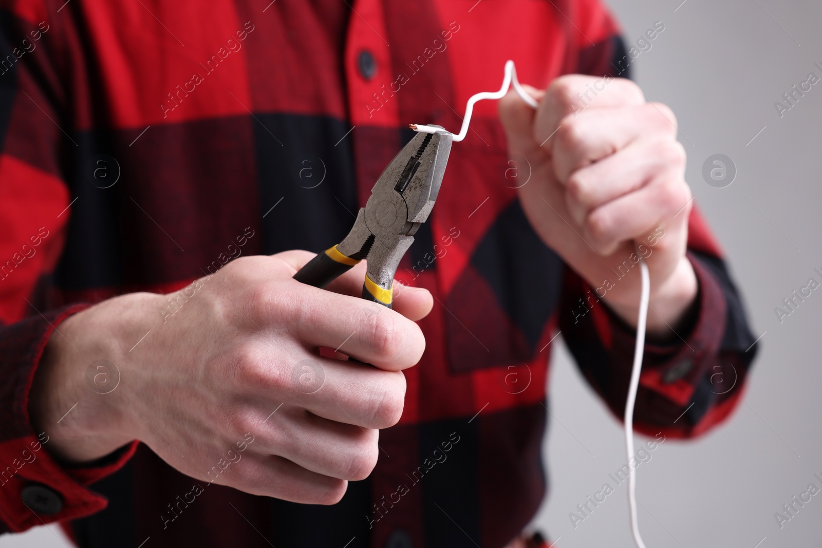 Photo of Young man holding pliers and wire on grey background, closeup