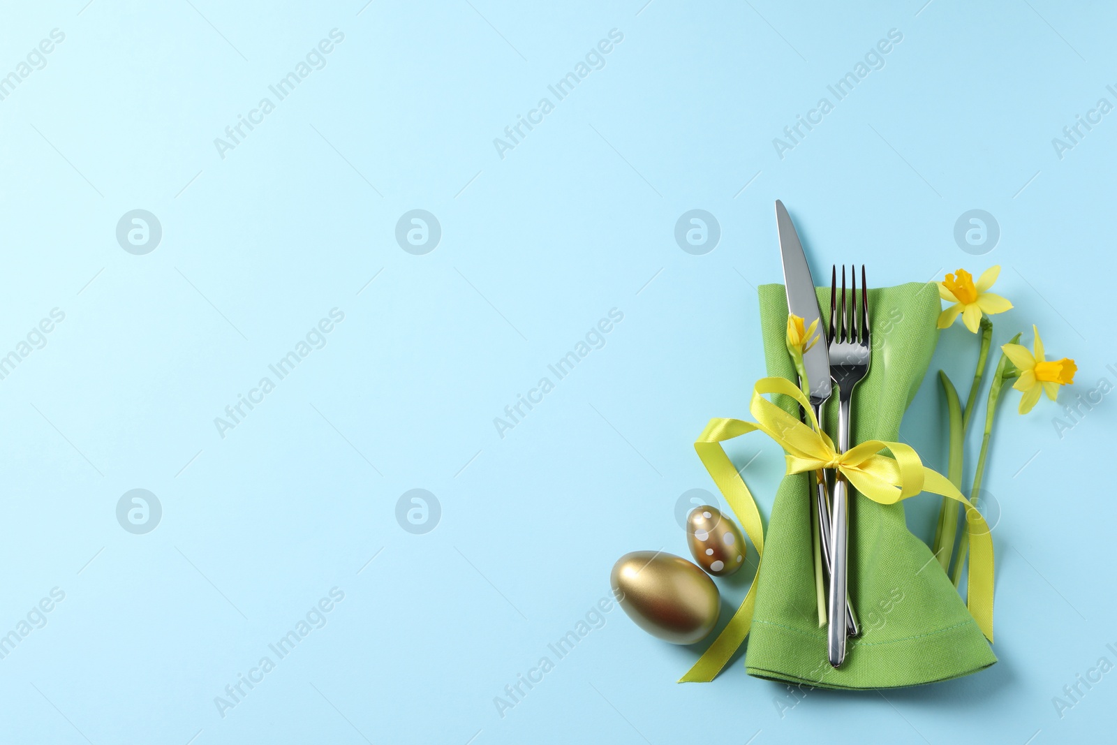 Photo of Cutlery set, Easter eggs and narcissuses on light blue background, flat lay with space for text. Festive table setting