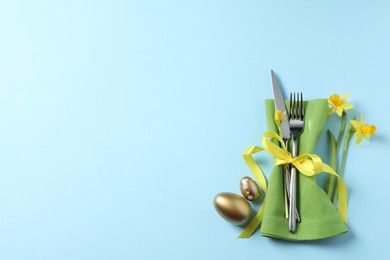 Photo of Cutlery set, Easter eggs and narcissuses on light blue background, flat lay with space for text. Festive table setting