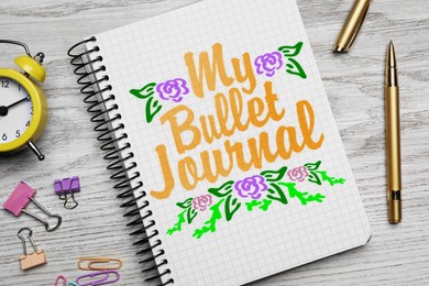 Image of Improve your productivity. Notebook with words My bullet journal, drawn flowers, stationery and alarm clock on white wooden table, flat lay