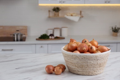 Photo of Basket with fresh onions on white marble table in modern kitchen. Space for text