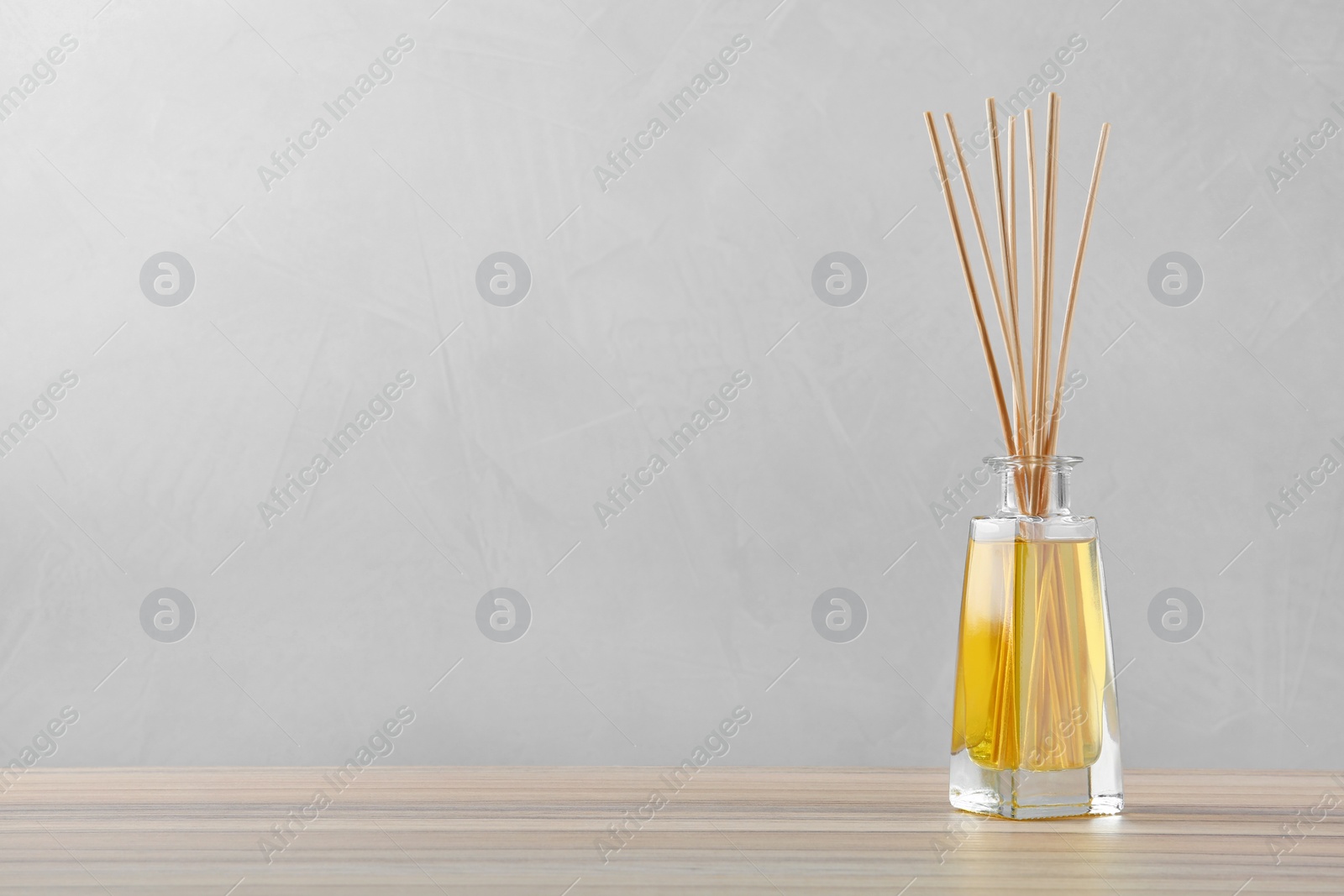 Photo of Reed air freshener on wooden table against grey background, space for text