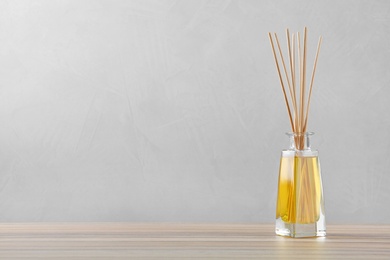 Photo of Reed air freshener on wooden table against grey background, space for text