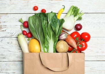 Photo of Paper bag with fresh vegetables on wooden background, flat lay