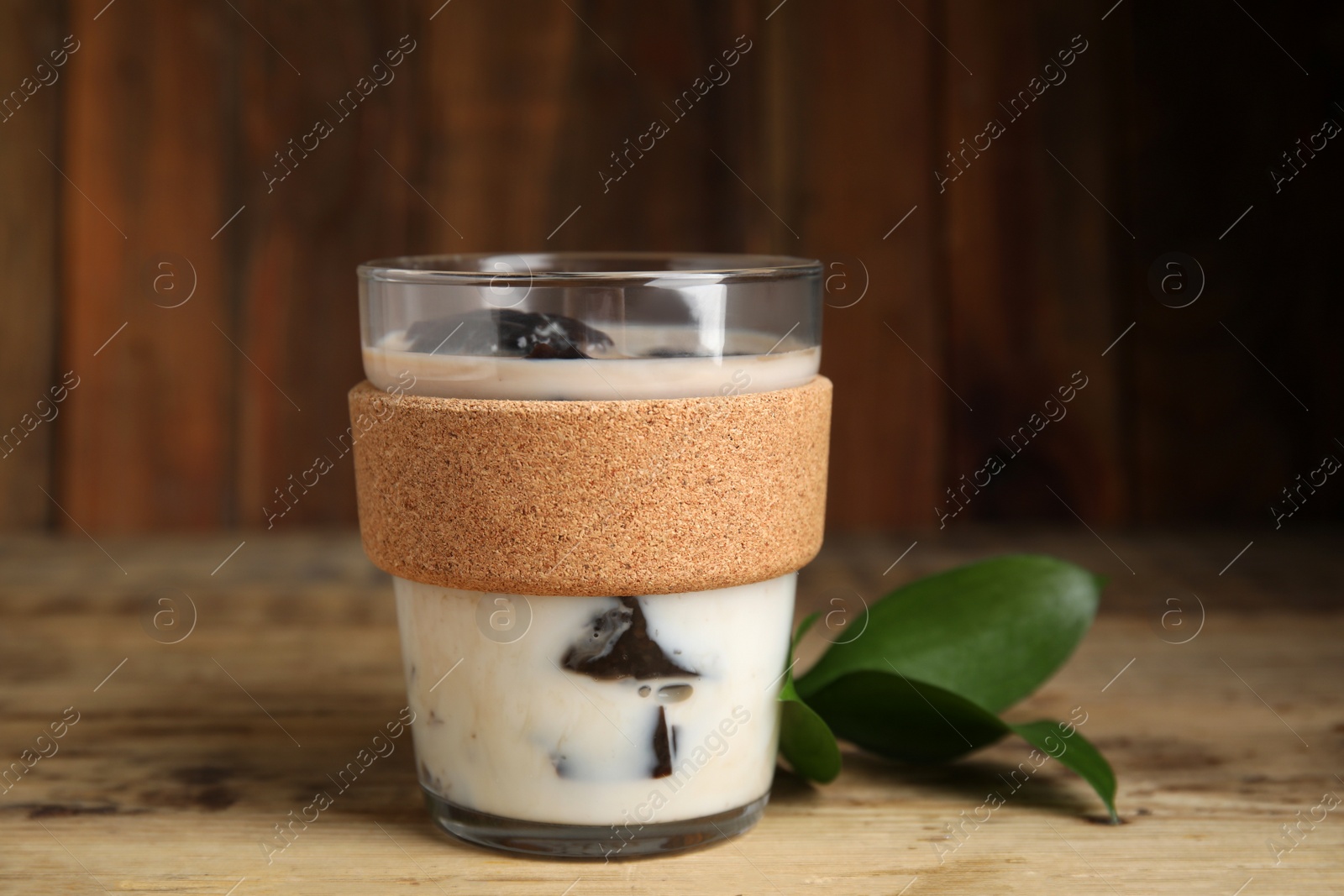 Photo of Glass of milk with grass jelly and green leaves on wooden table, closeup