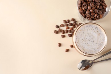 Photo of Refreshing iced coffee with milk in glass, beans and spoons on beige table, flat lay. Space for text