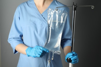 Nurse with IV infusion set on grey background, closeup