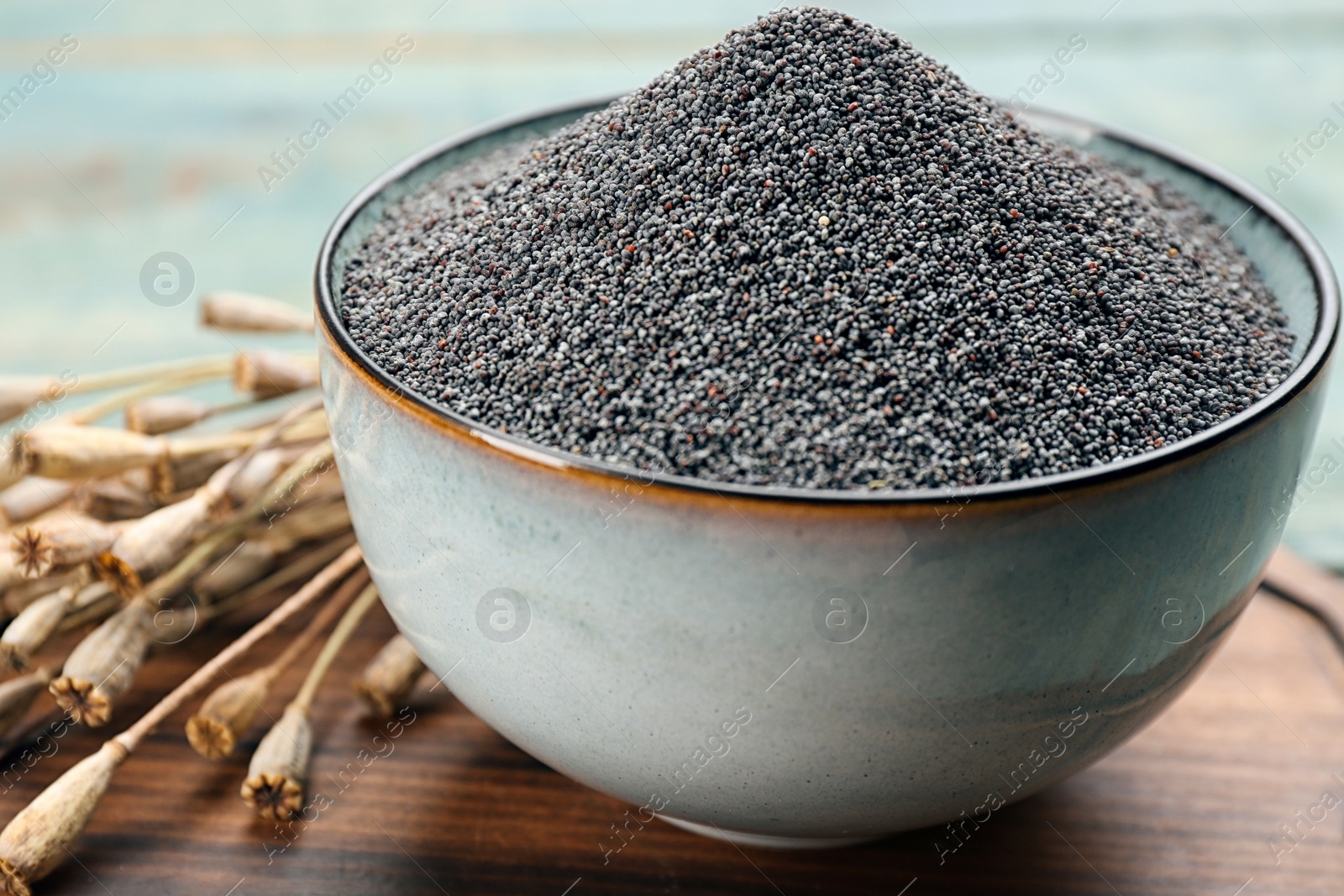 Photo of Poppy seeds in bowl on wooden board, closeup