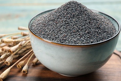 Poppy seeds in bowl on wooden board, closeup