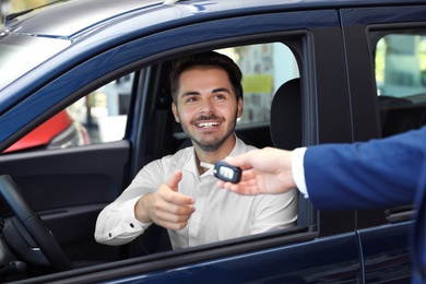 Photo of Young salesman giving car key to client in dealership