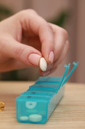 Woman taking pill from plastic box at wooden table indoors, closeup