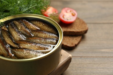 Tin can with tasty sprats on wooden table, closeup. Space for text