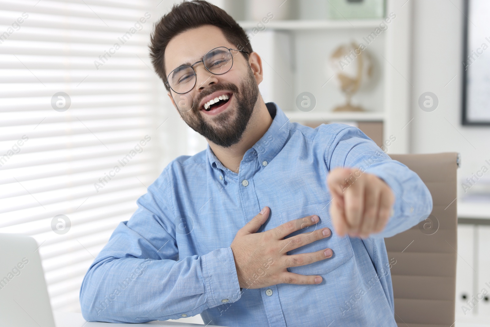 Photo of Handsome young man laughing while pointing at something in office