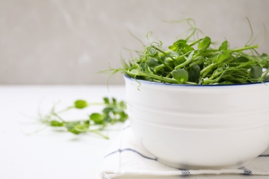 Bowl with fresh microgreen on white table, closeup. Space for text