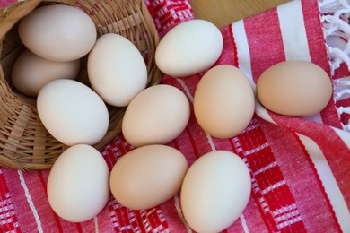 Photo of Overturned wicker basket with fresh raw eggs on table