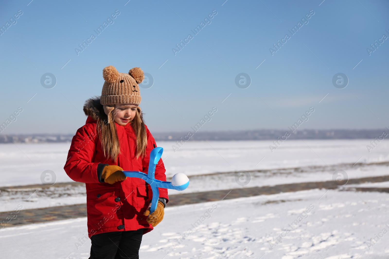 Photo of Cute little girl playing with snowball maker outdoors