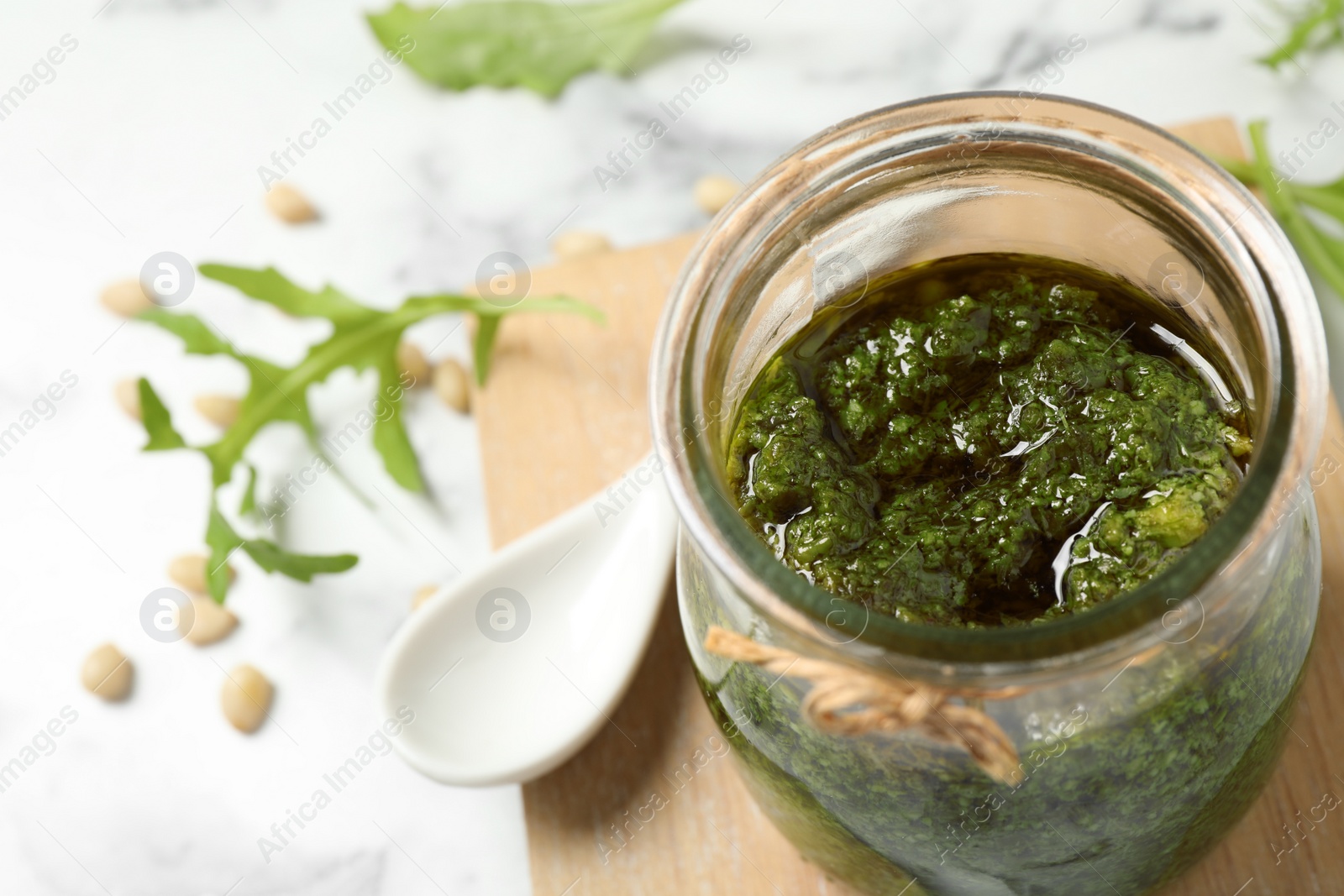 Photo of Jar of tasty arugula pesto on white table, closeup