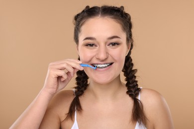 Smiling woman with dental braces cleaning teeth using interdental brush on beige background