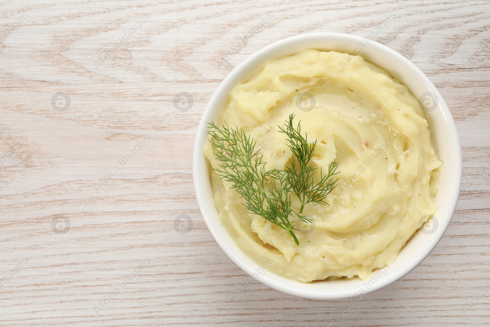 Photo of Bowl of tasty mashed potato with dill on wooden table, top view. Space for text