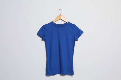 Photo of Hanger with blue t-shirt on light wall. Mockup for design