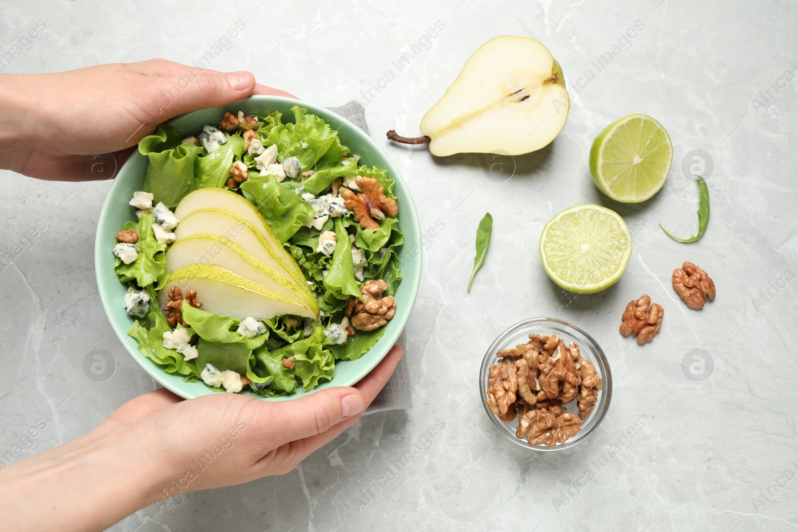 Photo of Woman holding tasty salad with pear slices at light grey marble table, top view