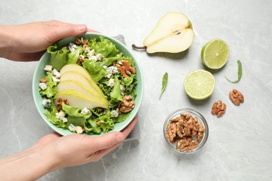 Photo of Woman holding tasty salad with pear slices at light grey marble table, top view