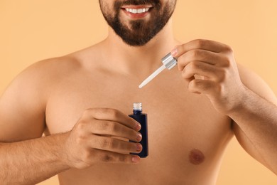 Photo of Man with cosmetic serum in hands on beige background, closeup