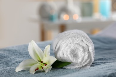 Photo of Spa composition with rolled towel and lily flower on massage table in wellness center