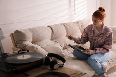 Photo of Young woman choosing vinyl disc to play music with turntable at home