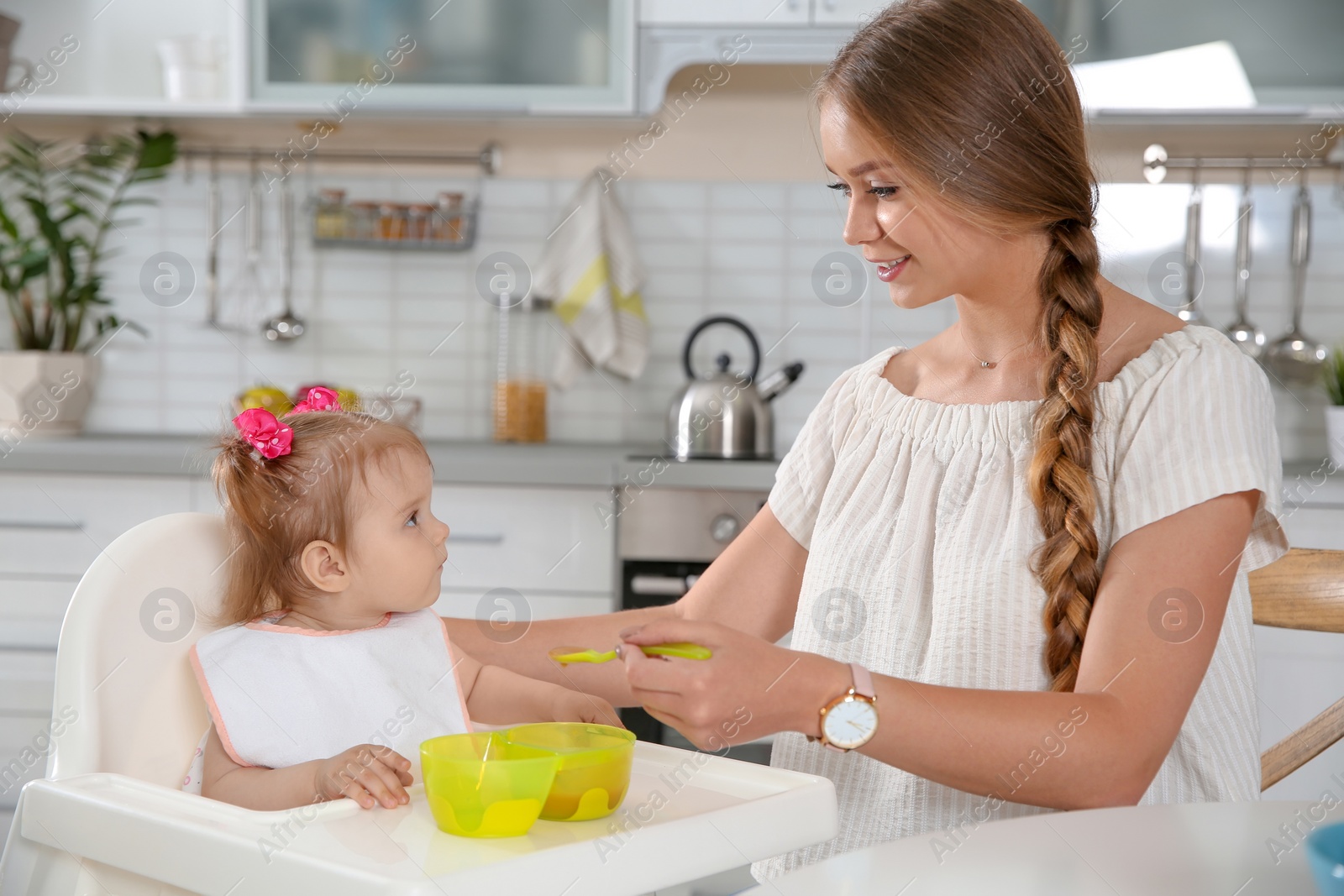 Photo of Mother feeding her little baby with healthy food in kitchen