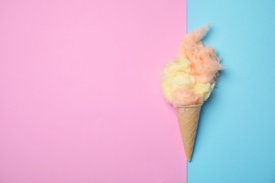 Photo of Ice cream cone with fluffy cotton candy and space for text on color background, top view