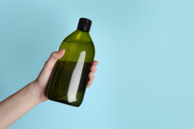 Photo of Woman holding shampoo bottle on turquoise background, closeup. Space for text