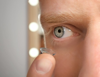 Photo of Young man putting contact lens into his eye, closeup