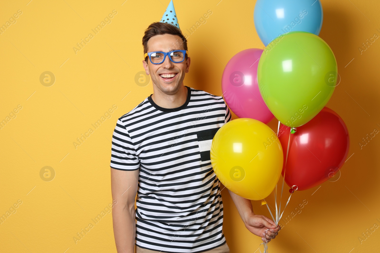 Photo of Young man with bright balloons on color background. Birthday celebration