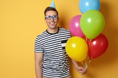 Young man with bright balloons on color background. Birthday celebration