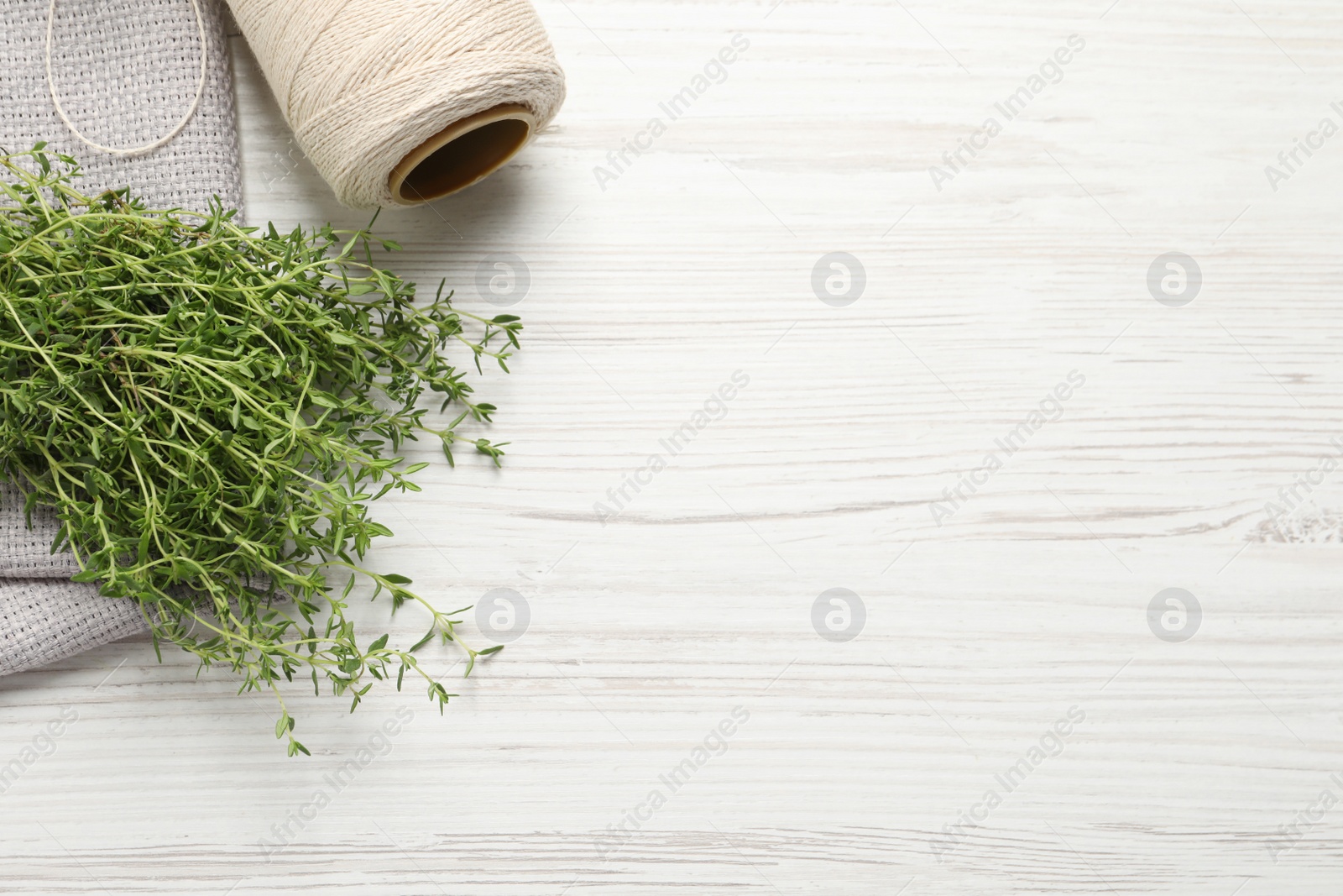 Photo of Bunch of aromatic thyme, napkin and twine on white wooden table, flat lay. Space for text