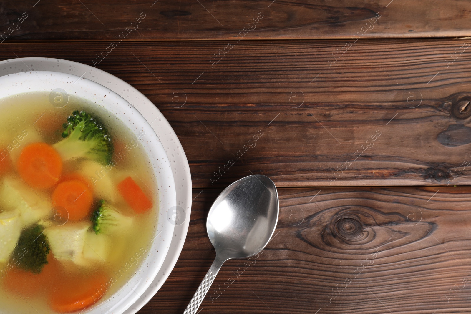 Photo of Tasty chicken soup with vegetables in bowl served on wooden table, top view. Space for text