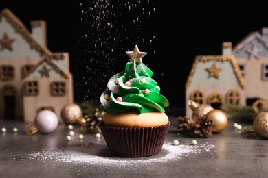 Sprinkling powdered sugar on Christmas tree shaped cupcake