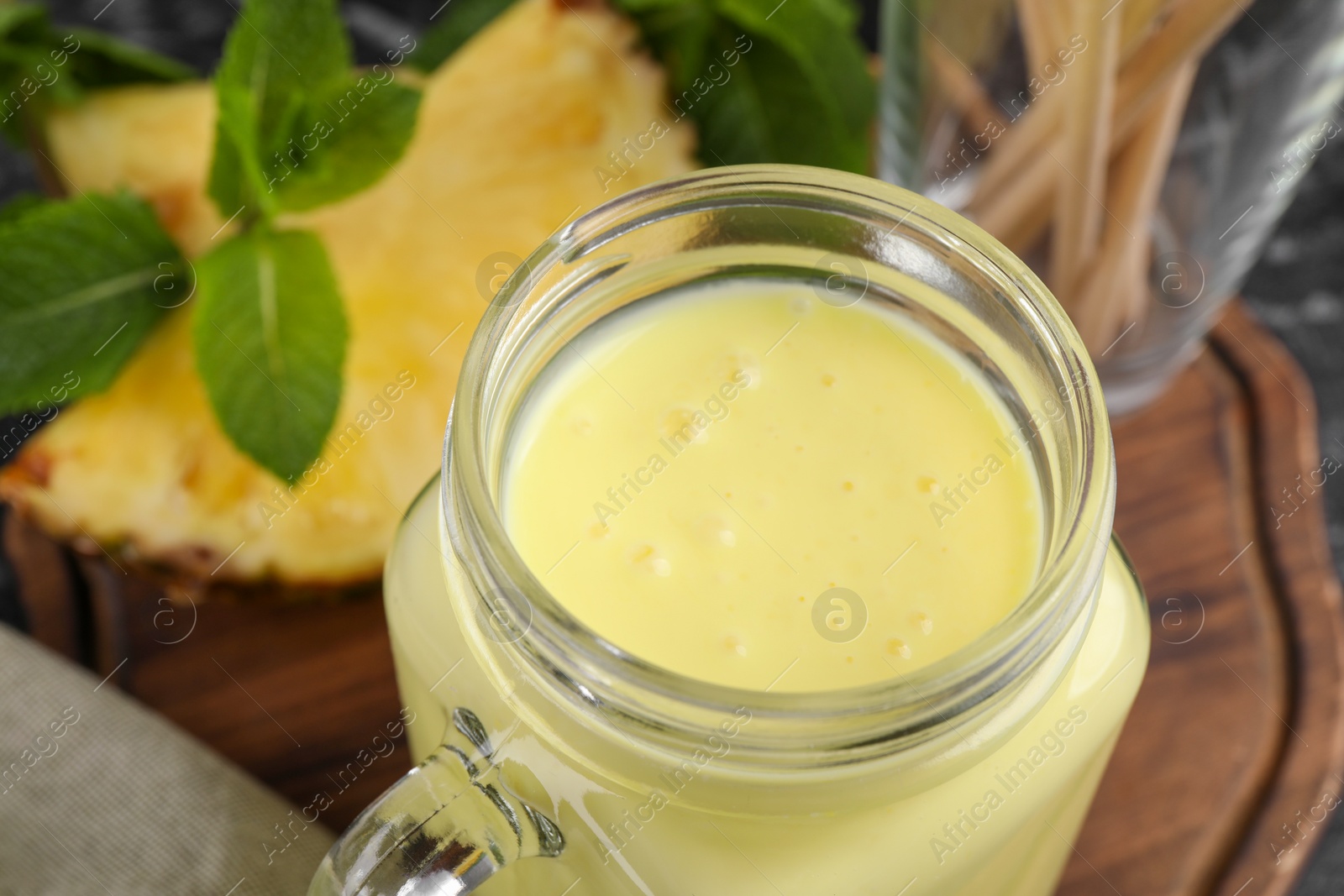 Photo of Tasty pineapple smoothie in mason jar on table, closeup