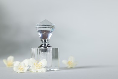 Photo of Aromatic perfume in bottle and beautiful jasmine flowers on grey background, space for text