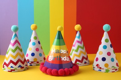 Different bright party hats with pompoms on color background