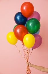 Woman holding bunch of bright balloons on color background, closeup. Celebration time