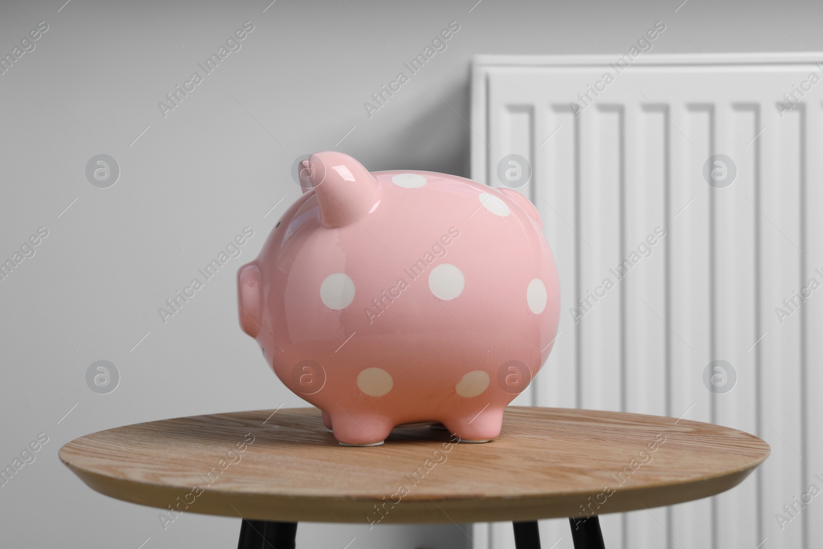 Photo of Piggy bank on wooden table near heating radiator