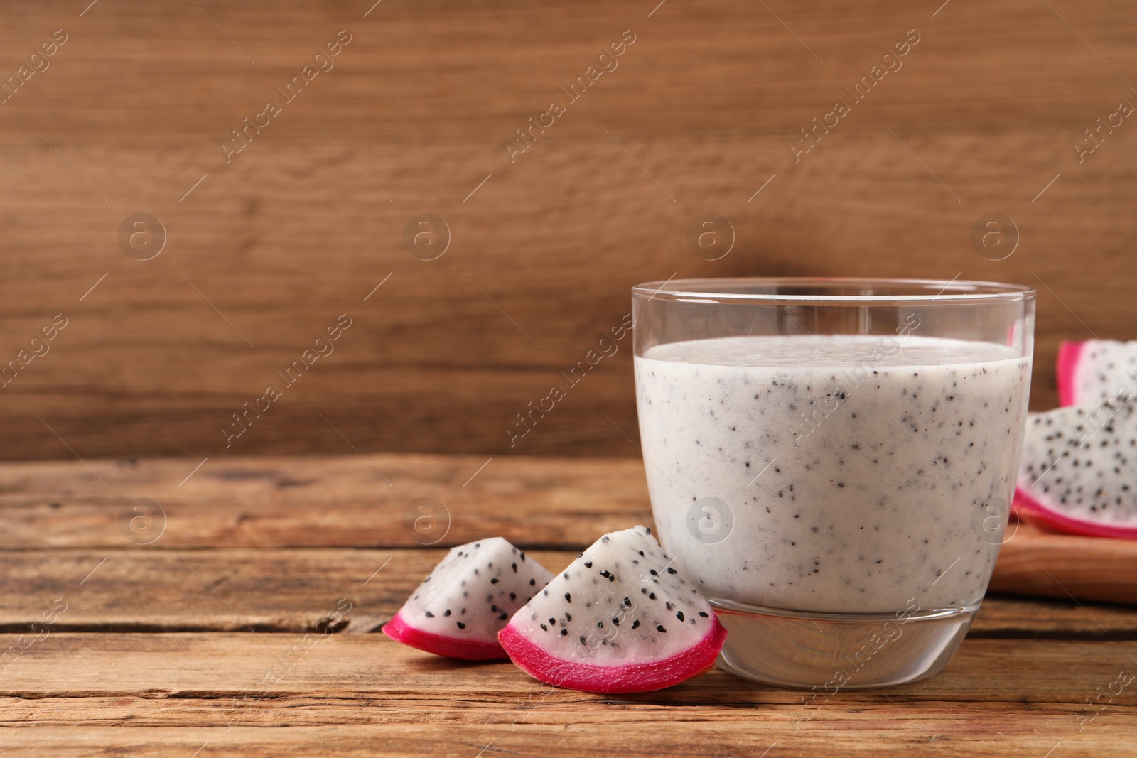 Photo of Glass of tasty pitahaya smoothie and fresh fruit on wooden table, space for text