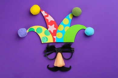 Photo of Flat lay composition with clown's face made of party glasses and hat on purple background