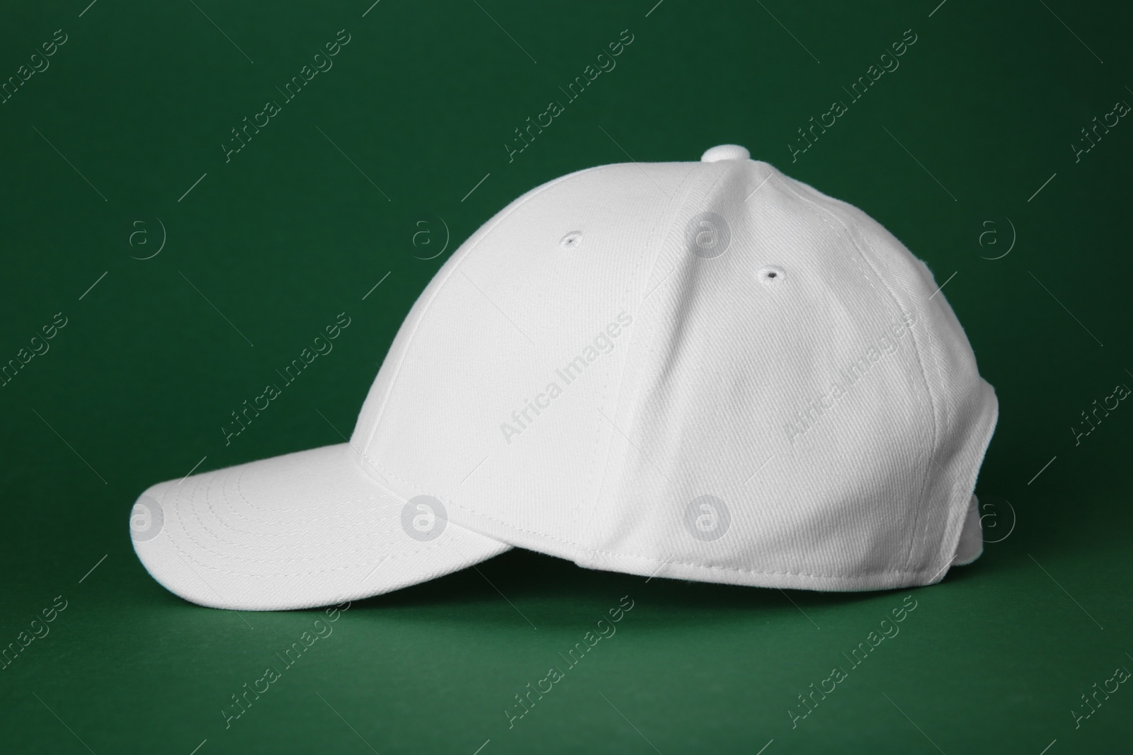 Photo of Stylish white baseball cap on dark green background