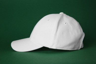 Stylish white baseball cap on dark green background